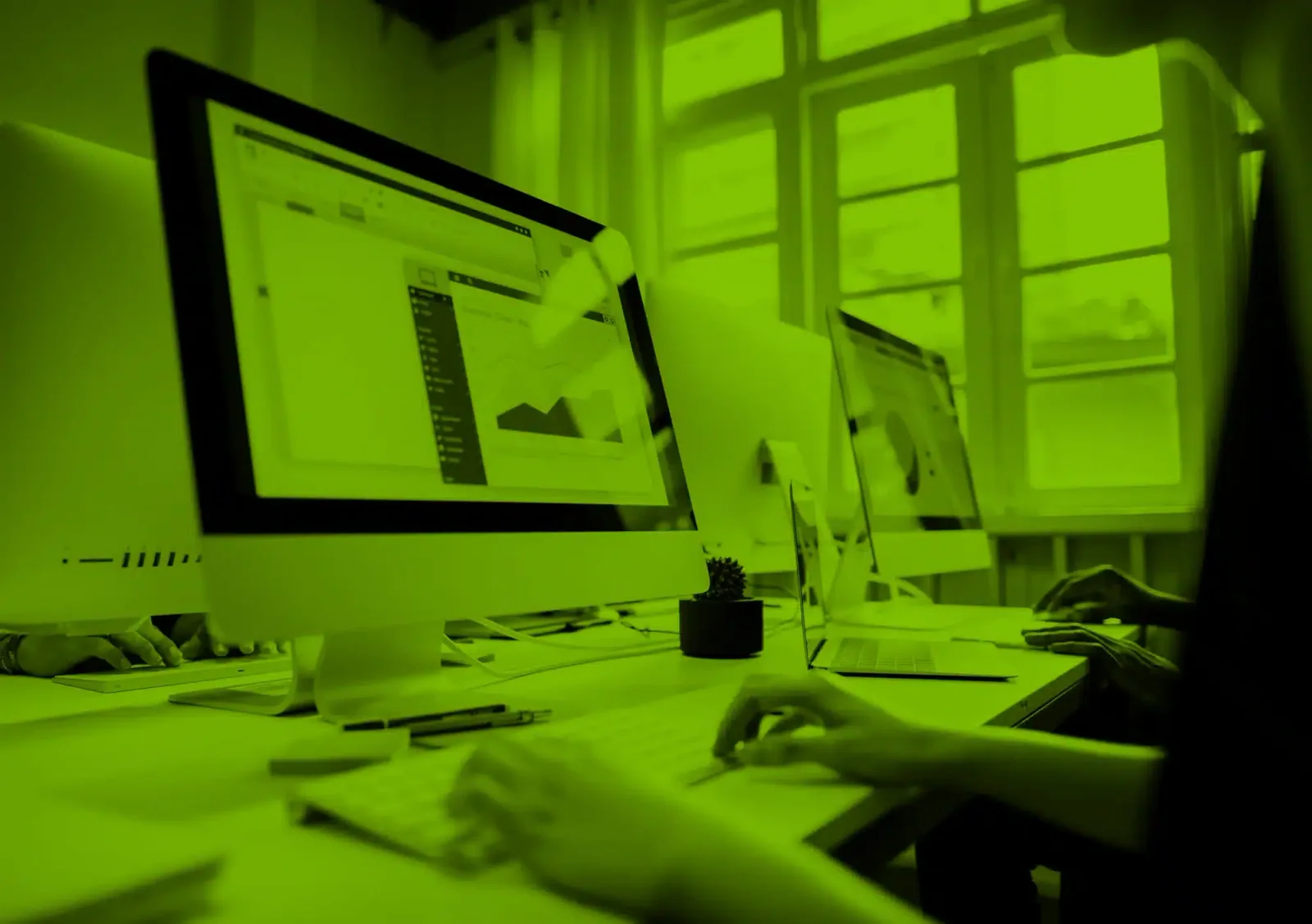 Green tinted photograph of desktop monitors and a laptop displaying website layouts, published by Ensalza.